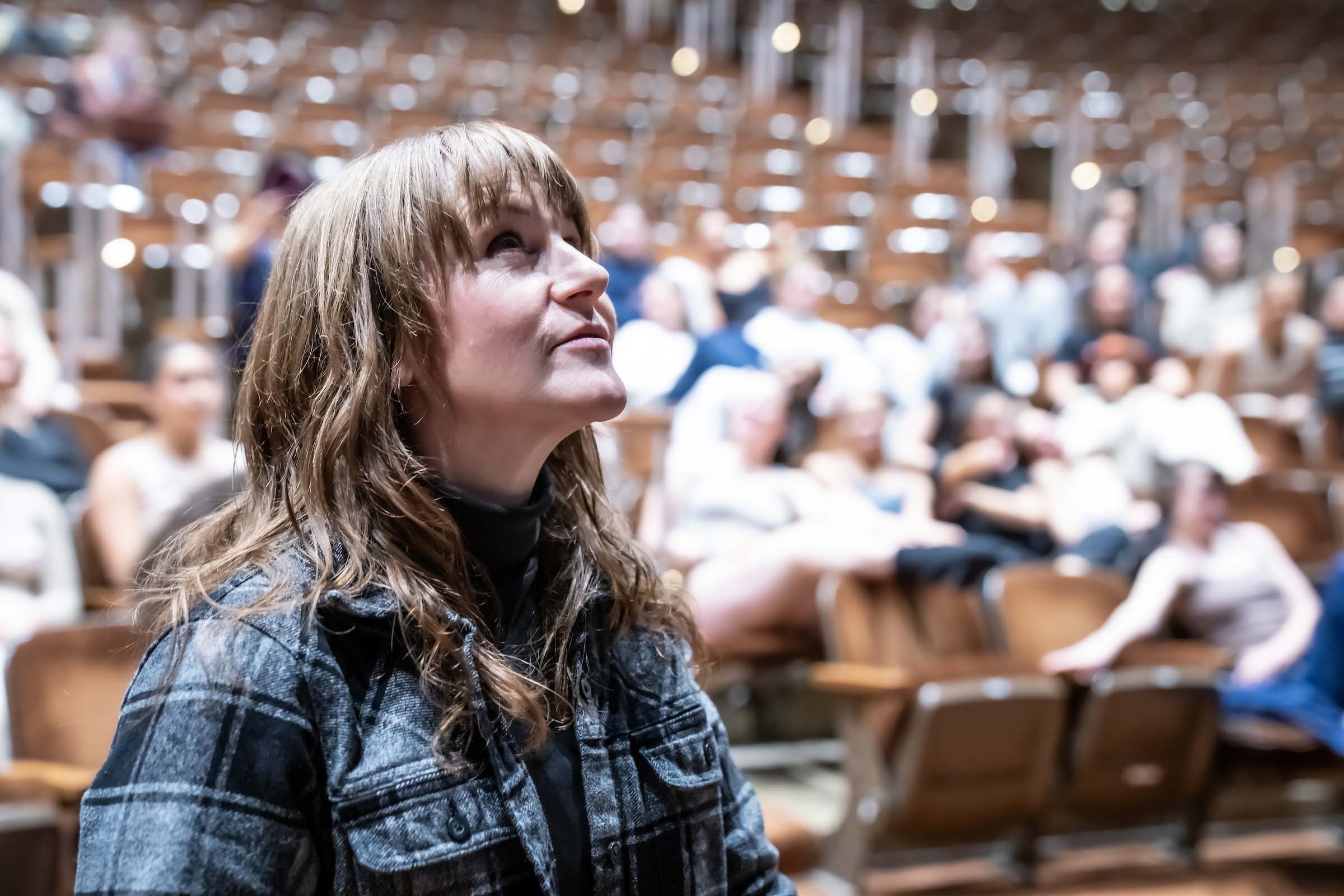 Candid photo of Jillian Hopper looking up in a performance hall, with students seated in the background.