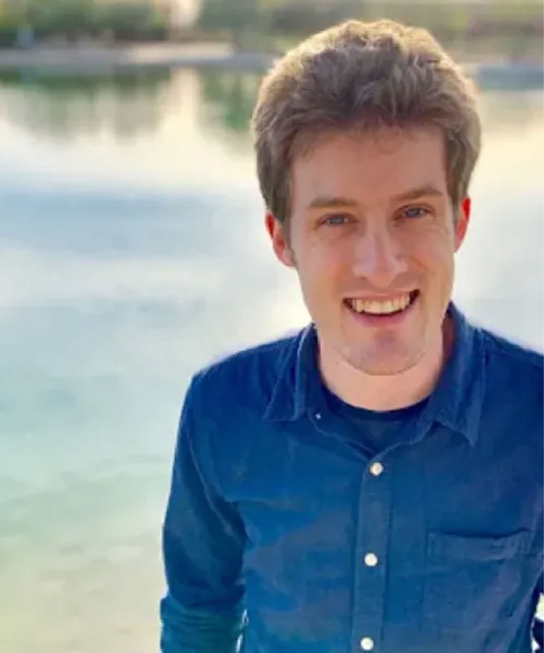 Outdoor portrait of Josh Graham with a small body of water in the background.