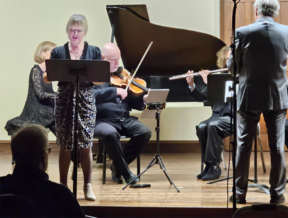 A vocalist and chamber orchestra perform on stage with a conductor.