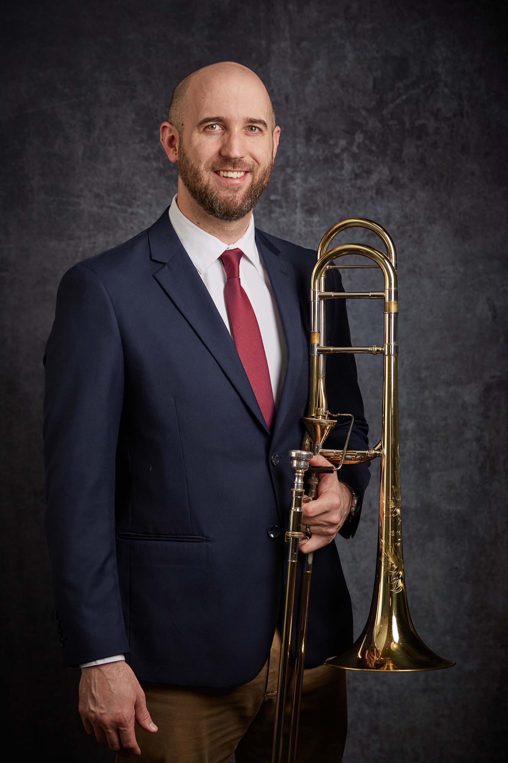 Studio portrait of Nate Musch standing with his trombone.