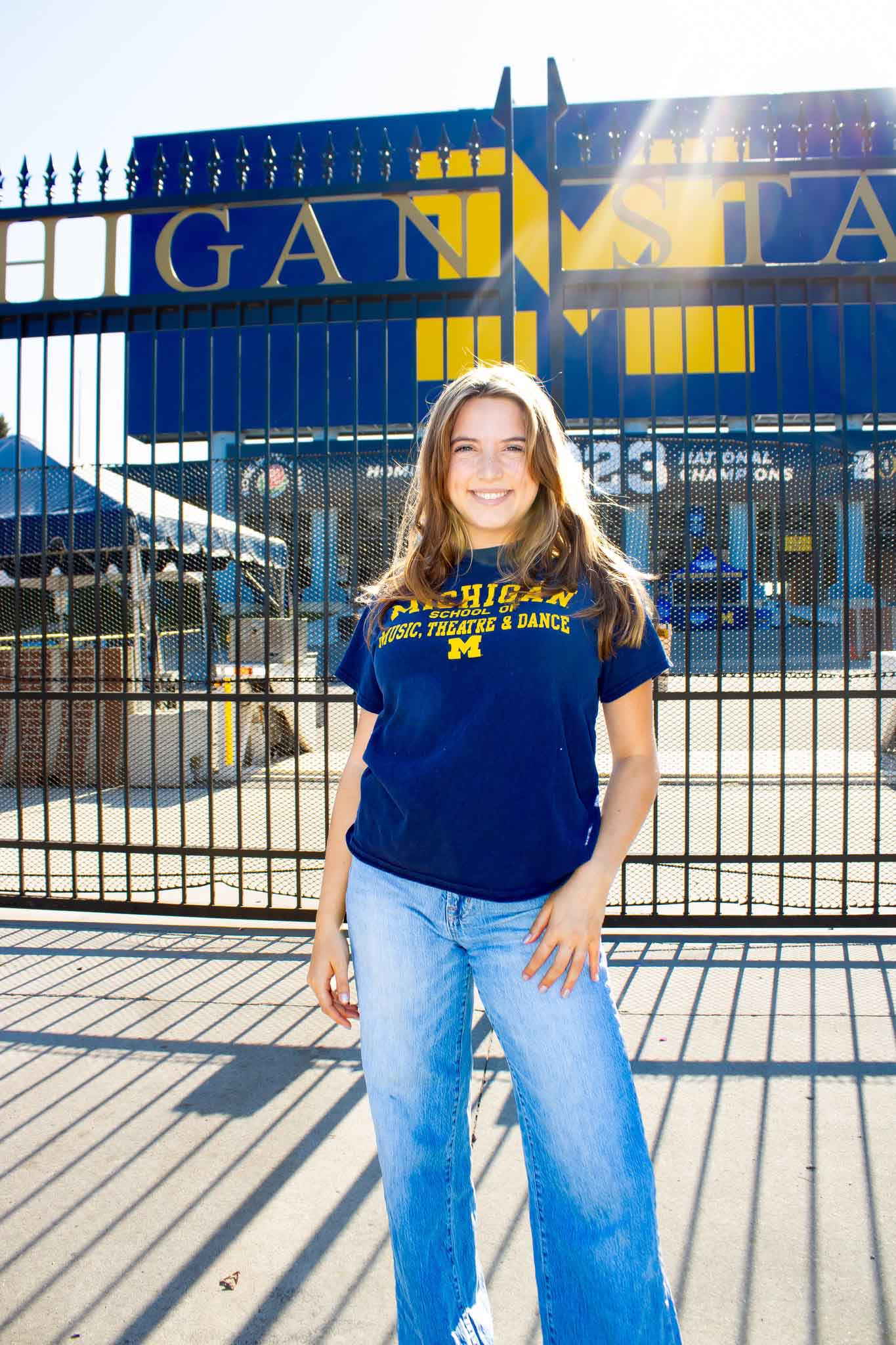 Standing portrait of Rachael Hymowitz outside the gates of Michigan Stadium, wearing an SMTD t-shirt.