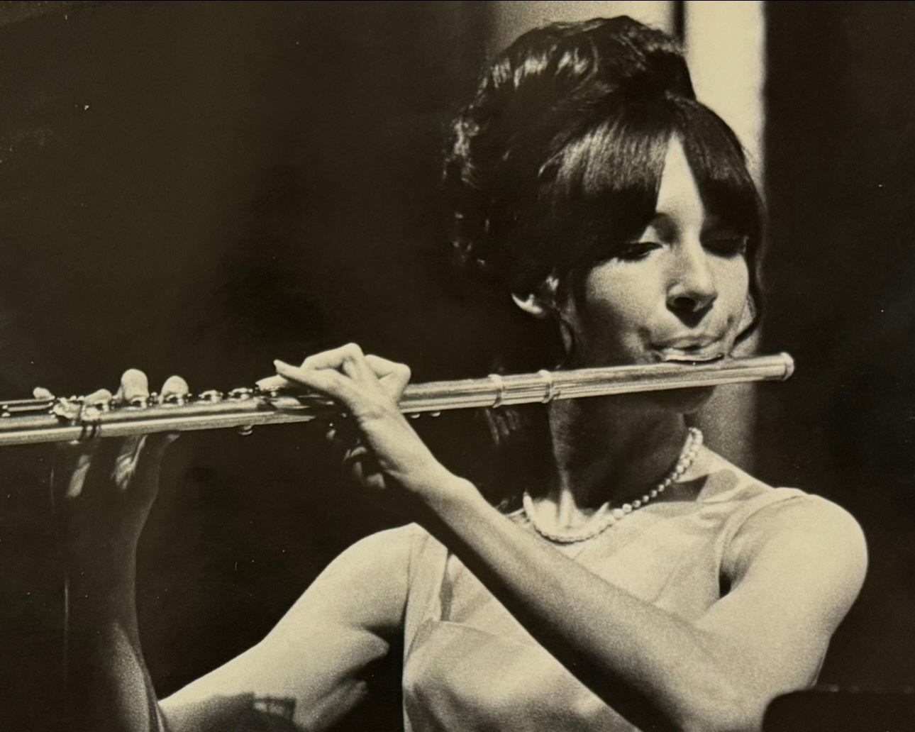 Greyscale vintage portrait of Sheryl Cohen playing the flute, wearing formal concert attire.