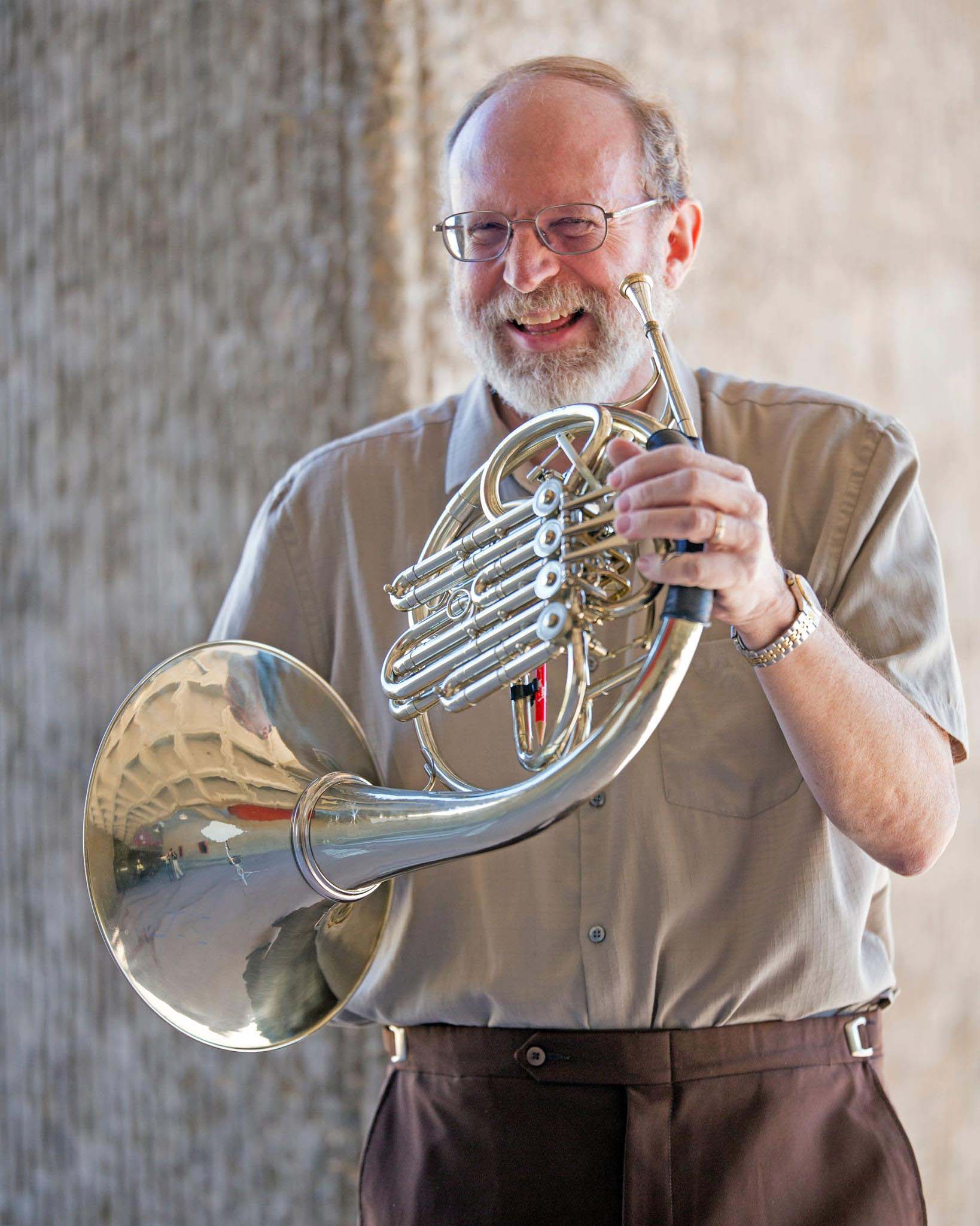 Candid photo of Steven Gross standing in a modern concrete space with his French horn.