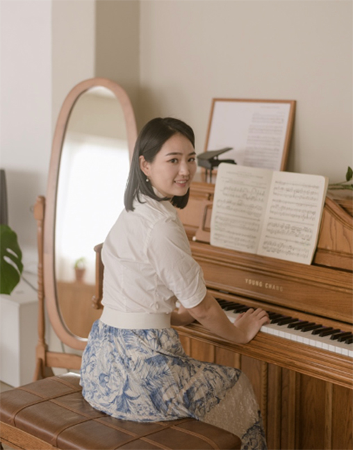 Taeyoon Ahn looks backwards while seated at an upright piano in playing position, with sheet music open.