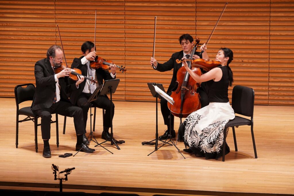 The Telegraph Quartet performs seated on stage, with all four members holding up their bows.