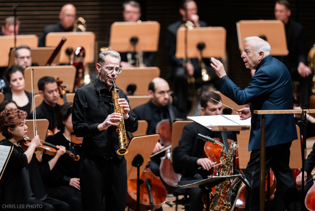 Timothy McAllister solos on soprano saxophone in a performance on stage with an orchestra and conductor.