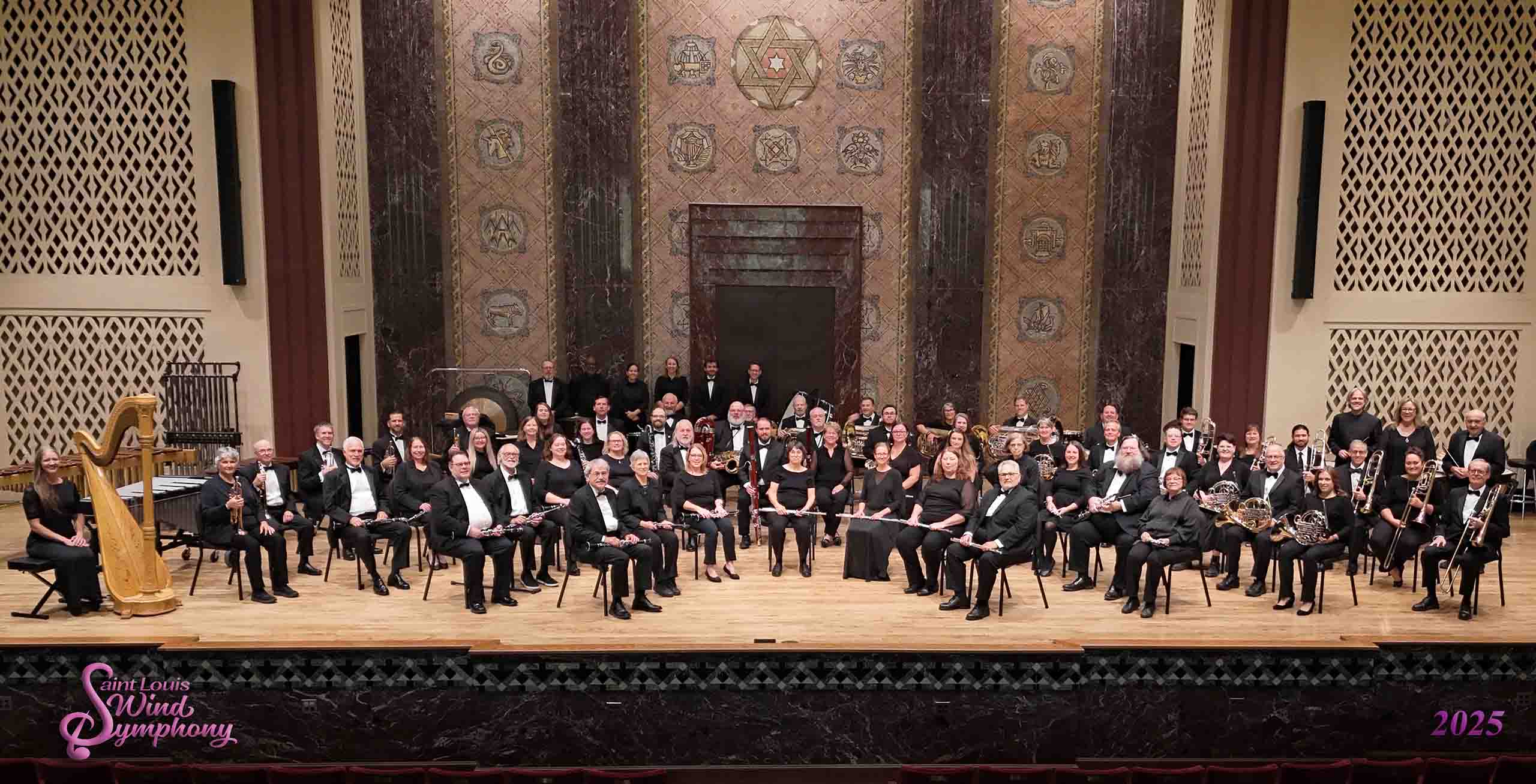 Formal group portrait of a professional orchestra seated on the stage of a concert hall.