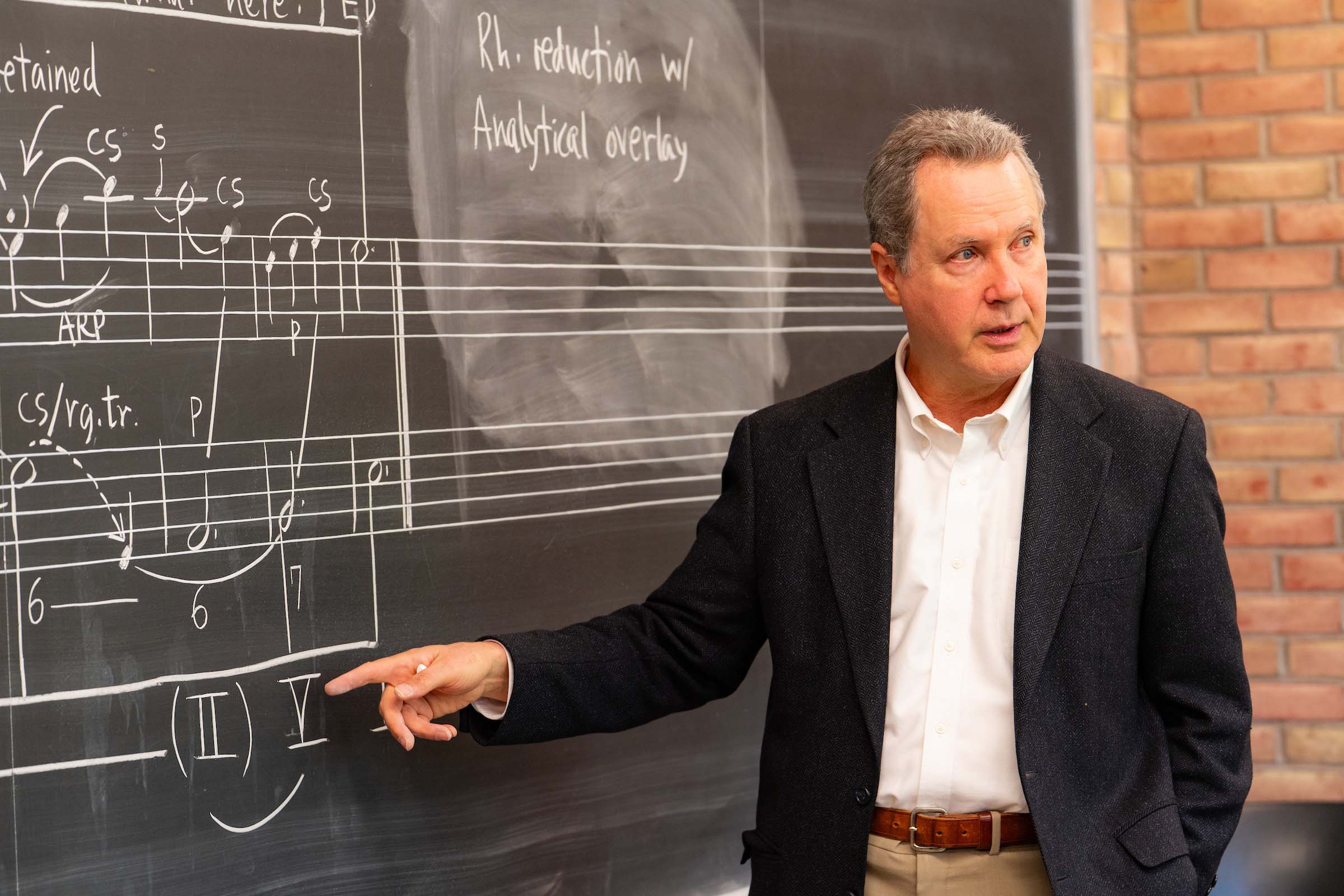 Wayne Petty stands teaching at a chalkboard with musical staff and notations.