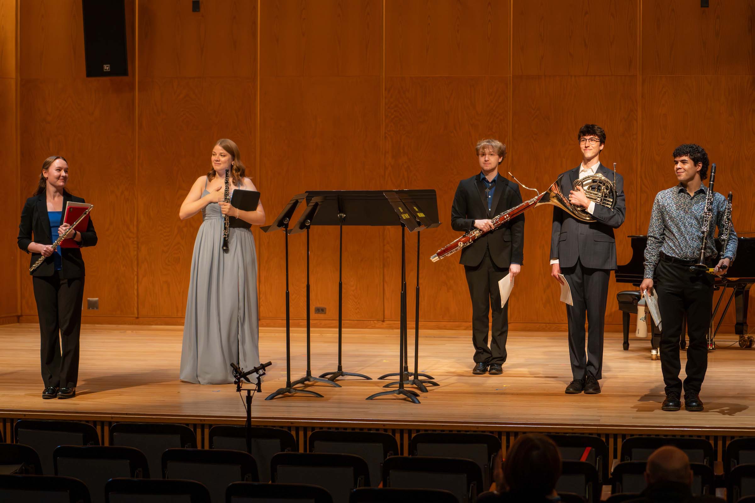 Five quartet performers stand on stage holding their wind instruments; all are attired formally in shades of blue, grey, and black.