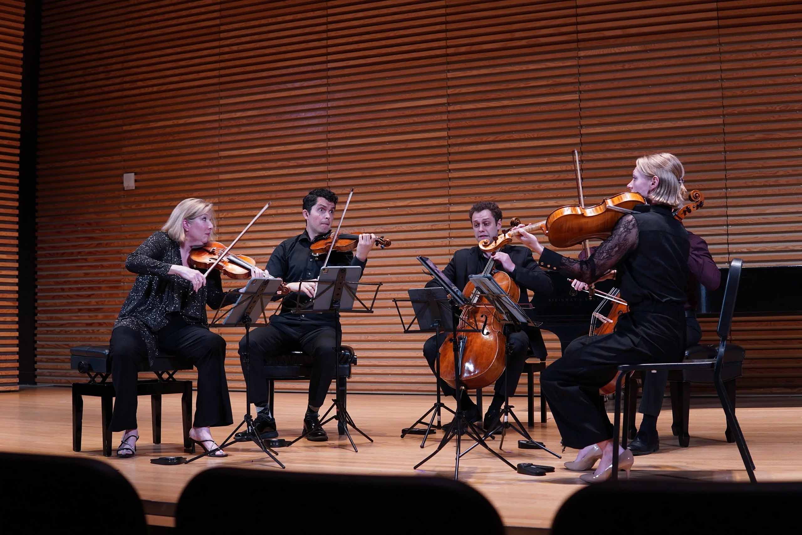 A string quintet performs on stage, wearing concert attire.