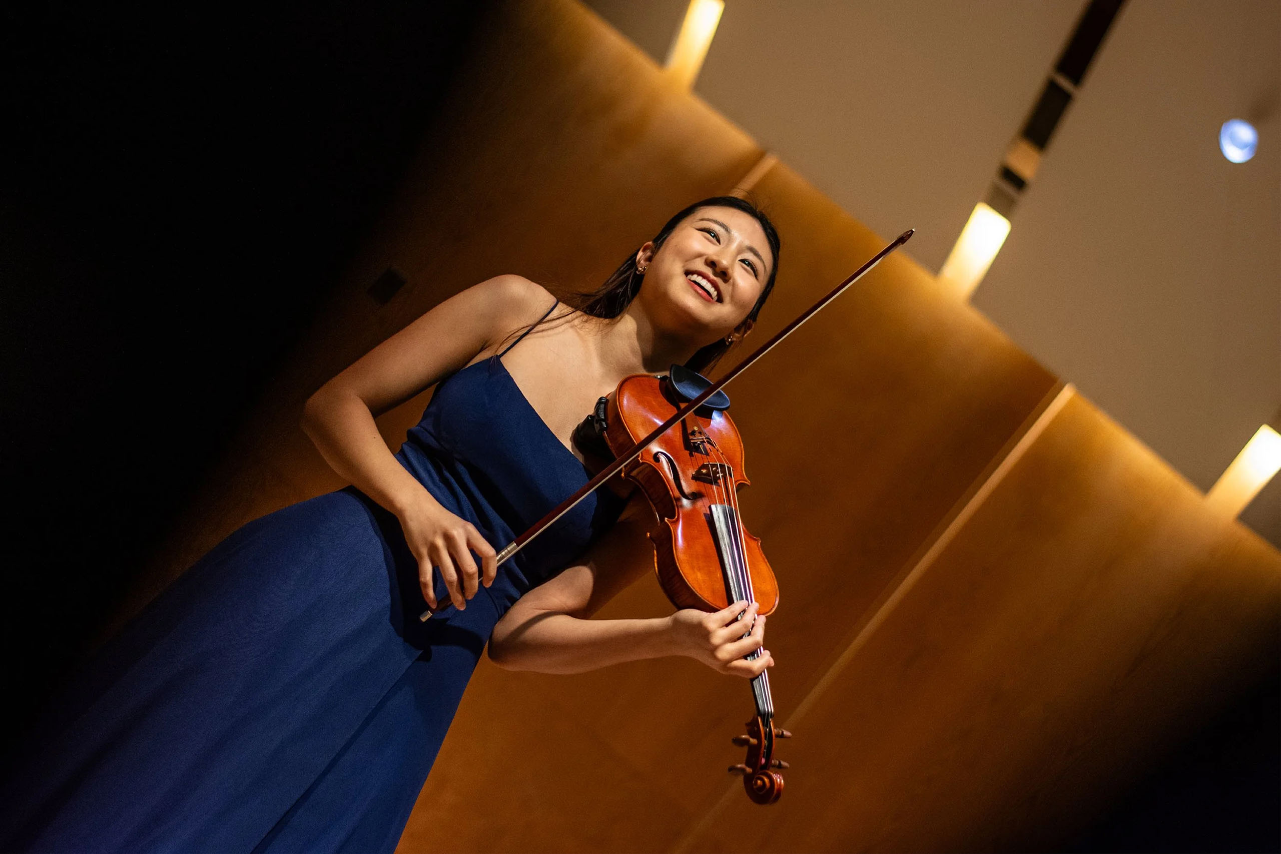 A string player wearing concert attire stands on stage with their instrument.