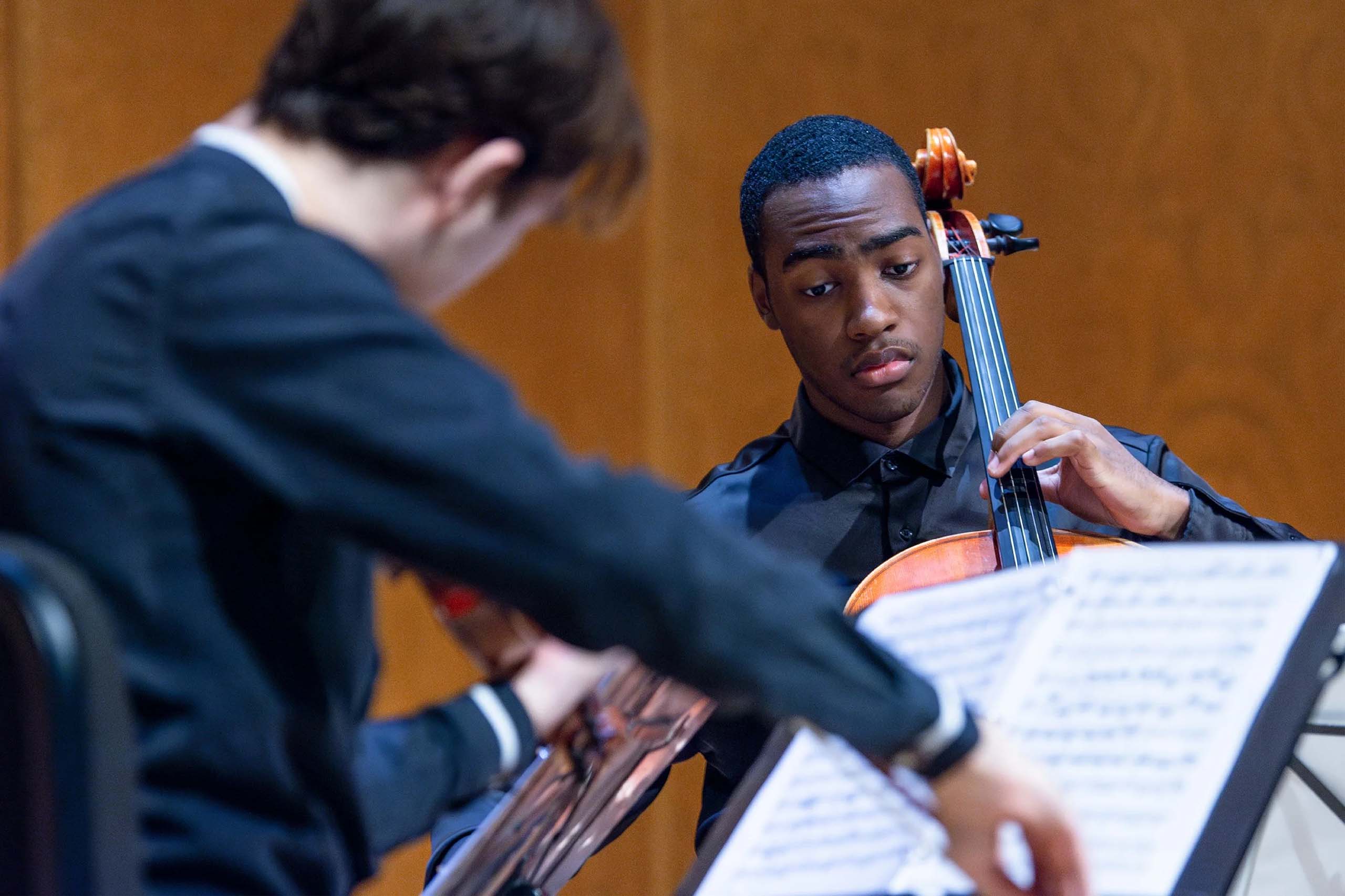 A string ensemble in performance, with two string players and sheet music visible.