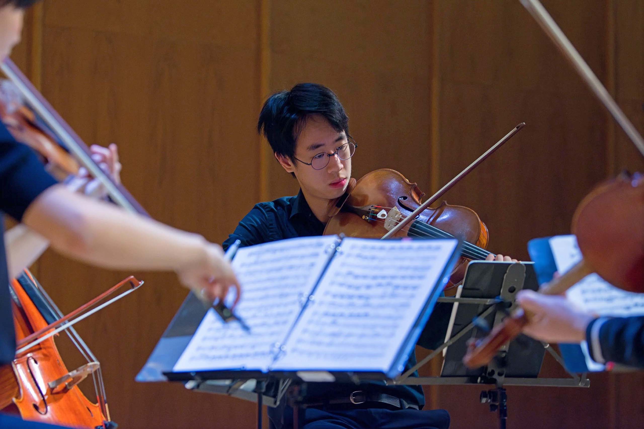 A string quartet performs using music on stands, and only one player's face is visible.