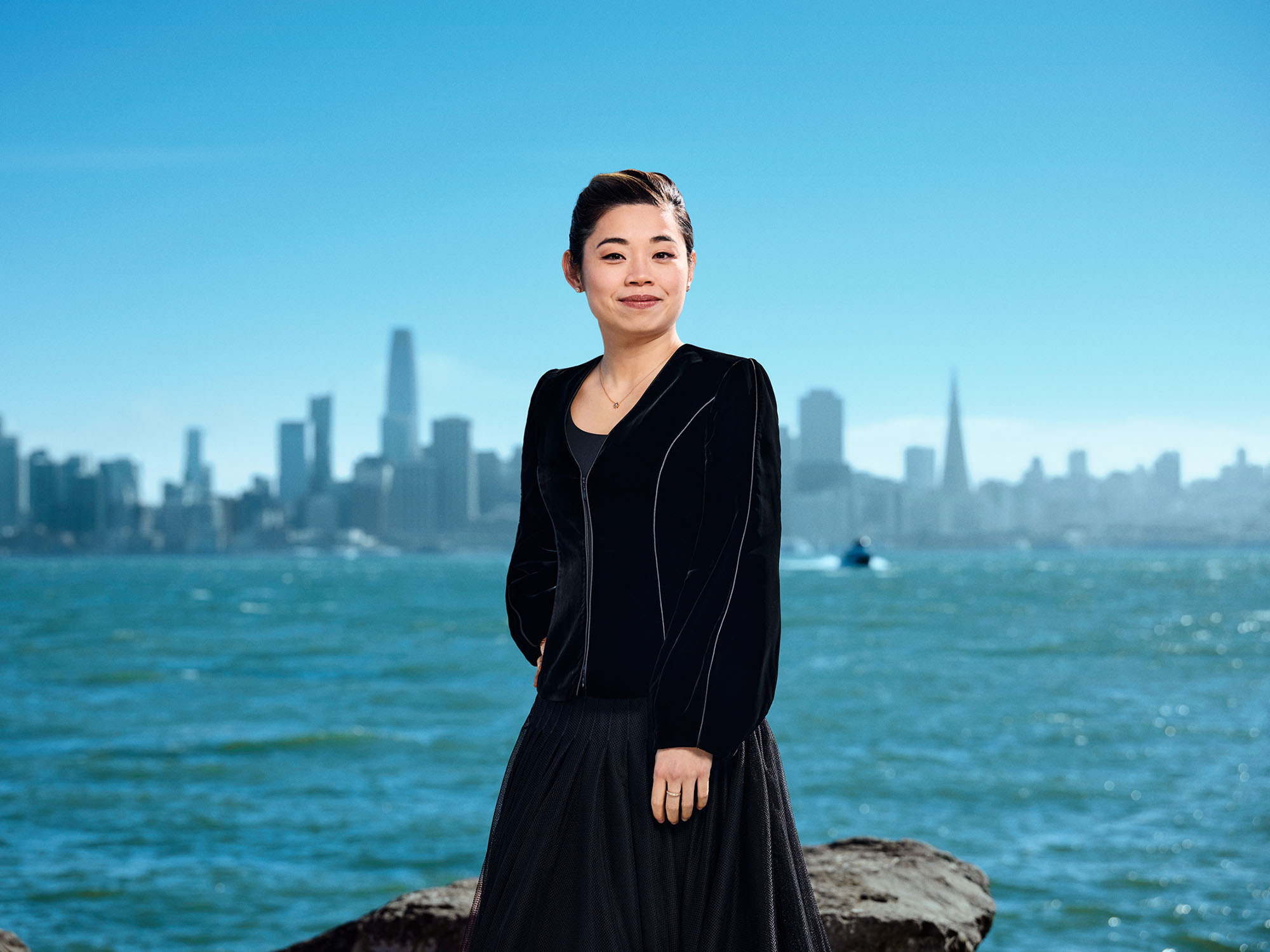 Portrait of Elim Chan standing outdoors next to the waters of the bay with the San Francisco skyline in the background.