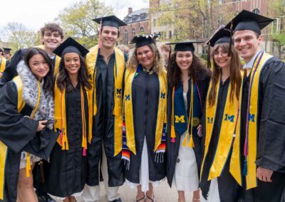 A group of 8 graduates wearing academic regalia pose standing together on the Ingalls Mall.