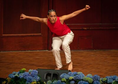 Kiana "KC" Cook performs a dance on stage, with arms held out wide and legs bent.