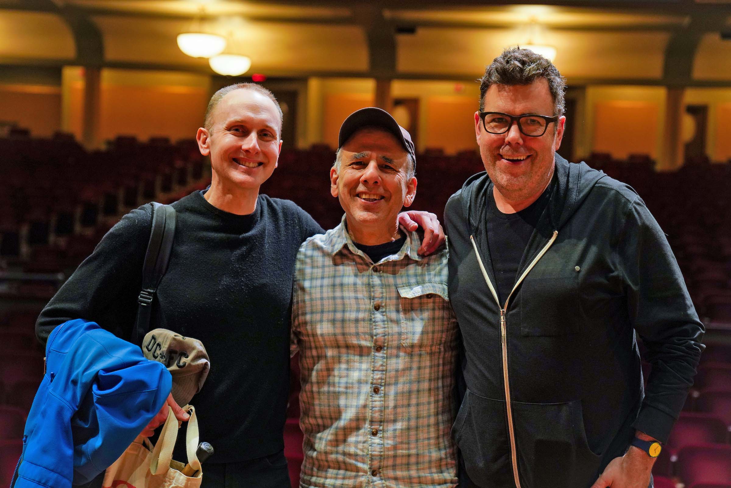 Three people pose standing together in the Hill Auditorium house.
