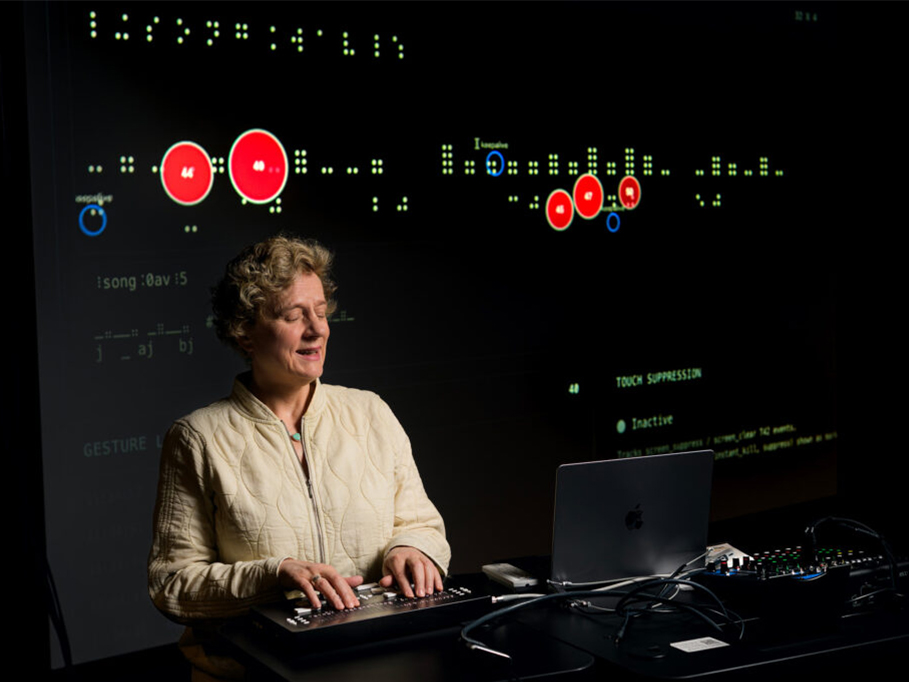 Sile O'Modhrain speaks with her hands placed on a Codex refreshable Braille device, and a Braille display projected on the wall in the background.