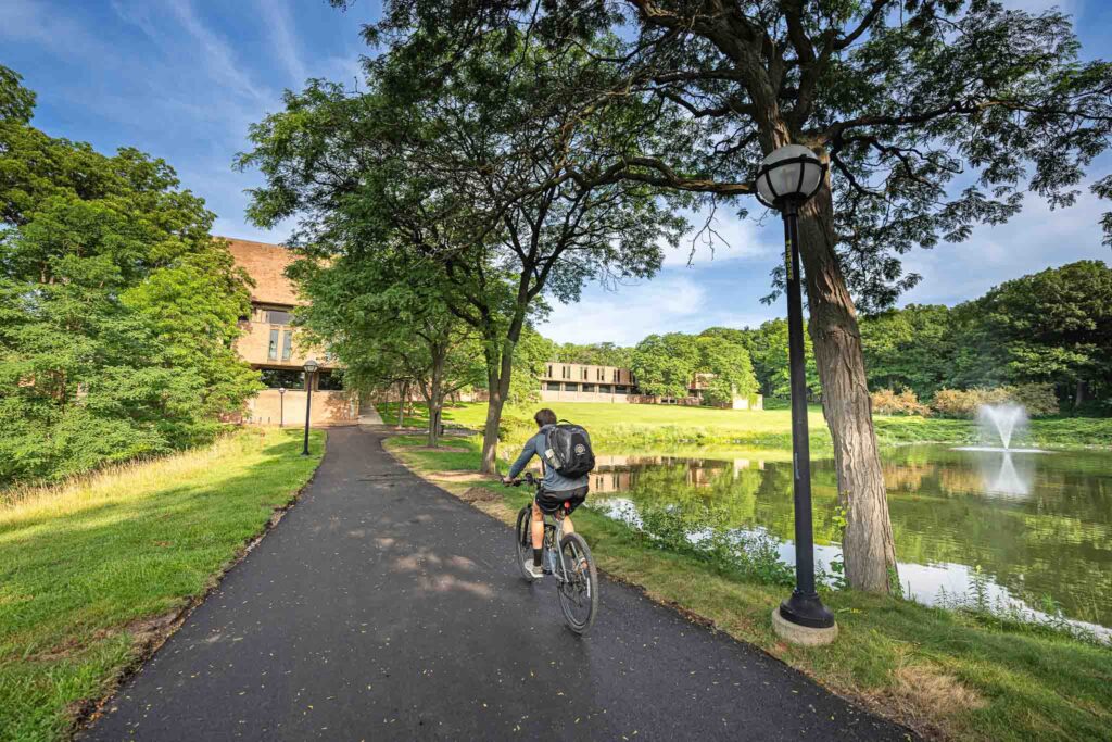 A biker takes the path towards the SMTD Moore Building on a summer day, with the SMTD Pond at right.
