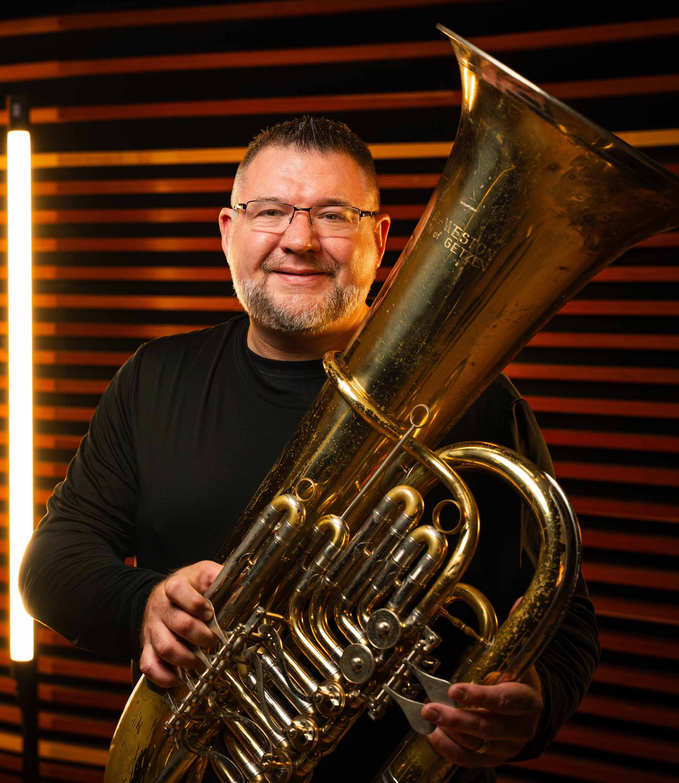 Standing portrait of Alex Lapins wearing black, holding his tuba.