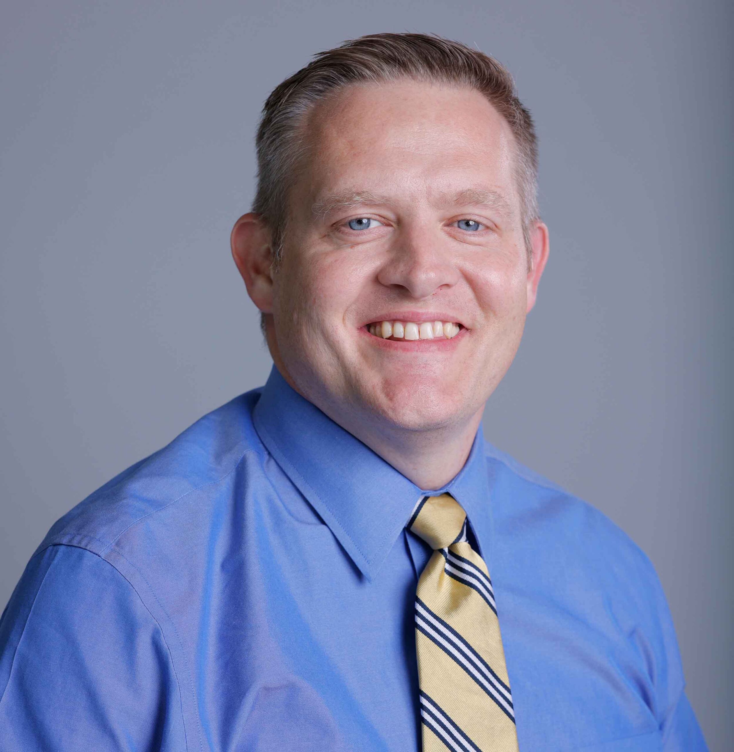 Studio headshot of Brandon Bascom wearing a blue shirt and yellow tie.
