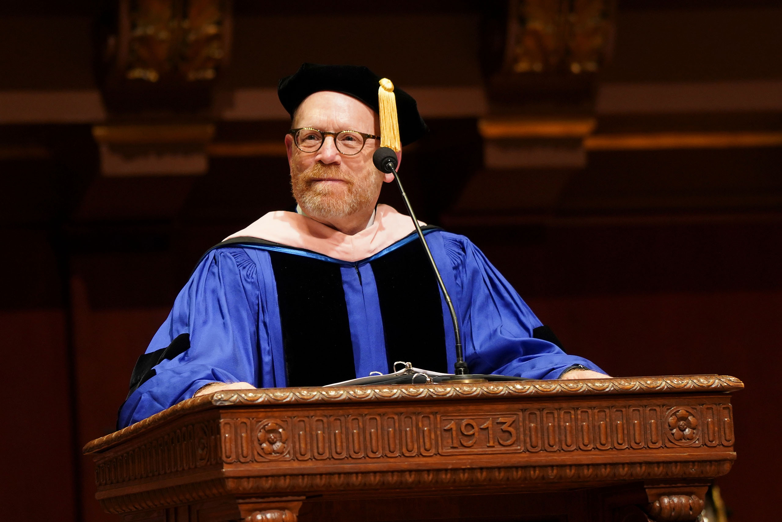 Dean Gier speaks at the historic podium in Hill Auditorium, attired in academic regalia for Commencement.