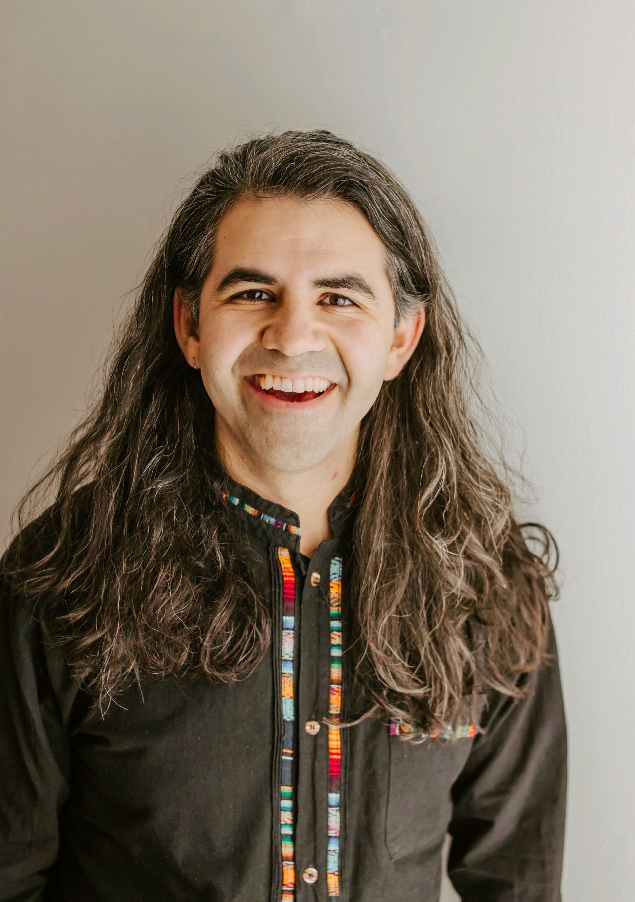 Portrait of Eric Reyes standing, attired in a black shirt with colorful trim.