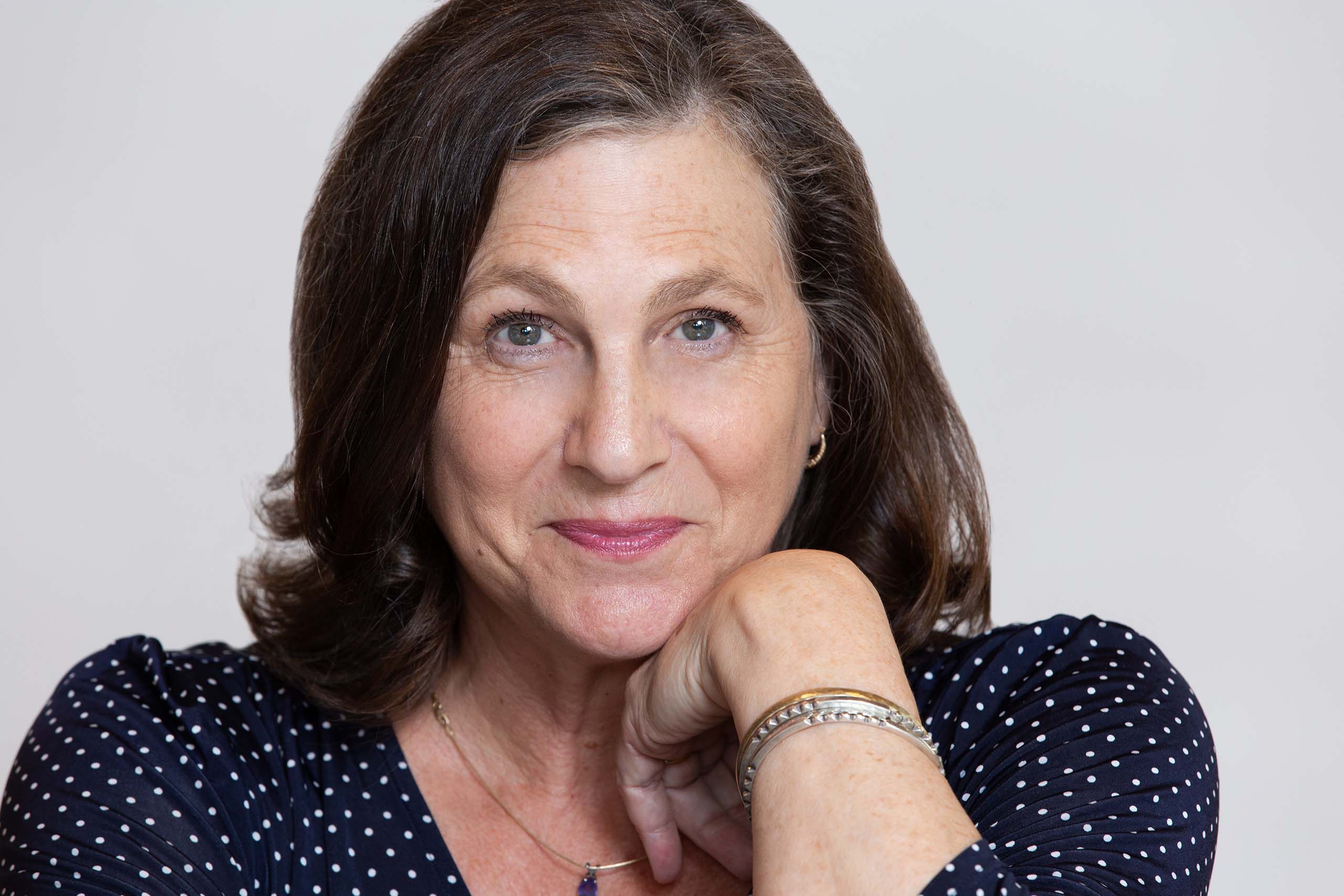Studio headshot of Janet Lilly, with chin resting on her wrist, attired in a black polka dot blouse. 