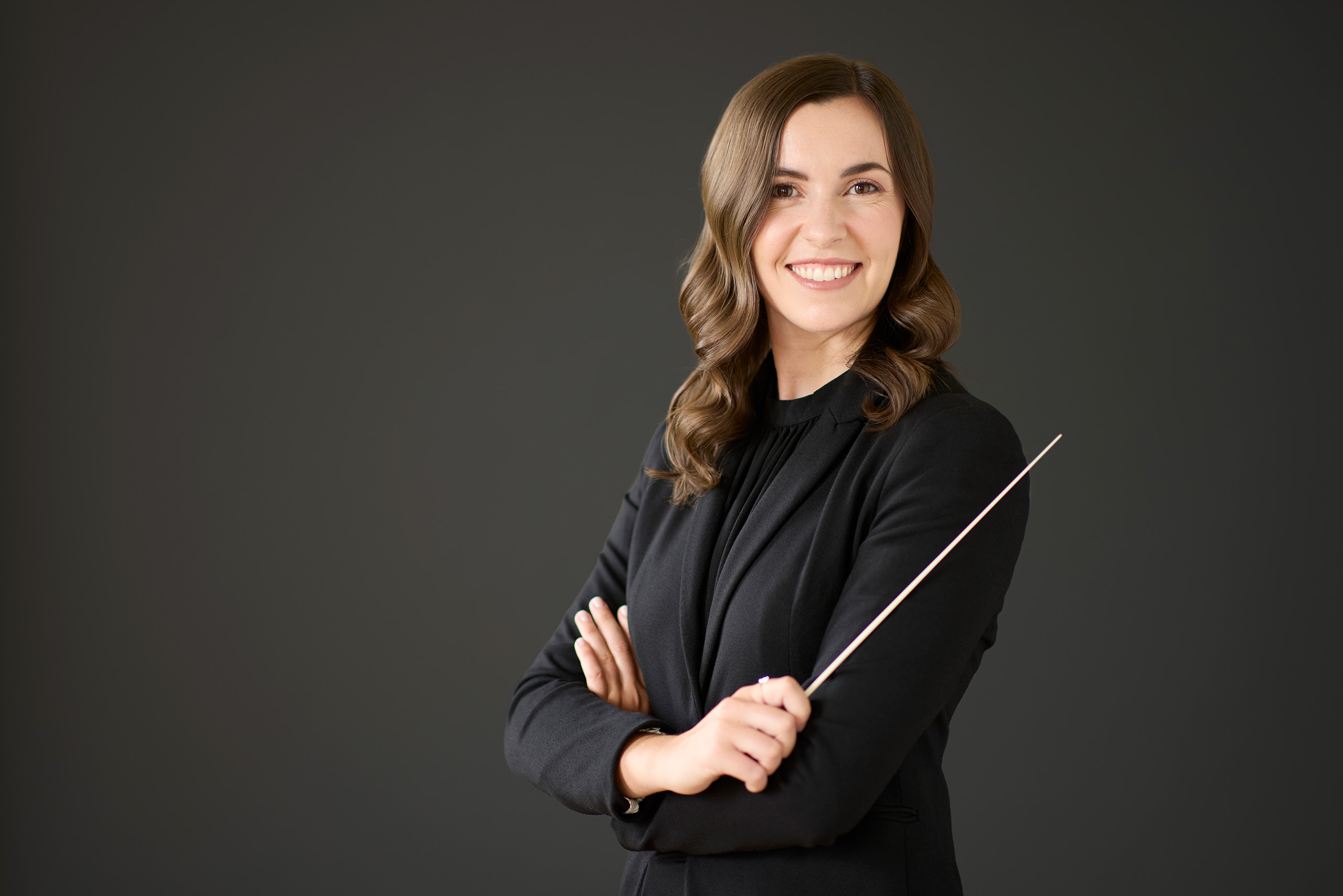 Formal studio portrait of Jen Hepp, holding a conductor's baton with arms folded.