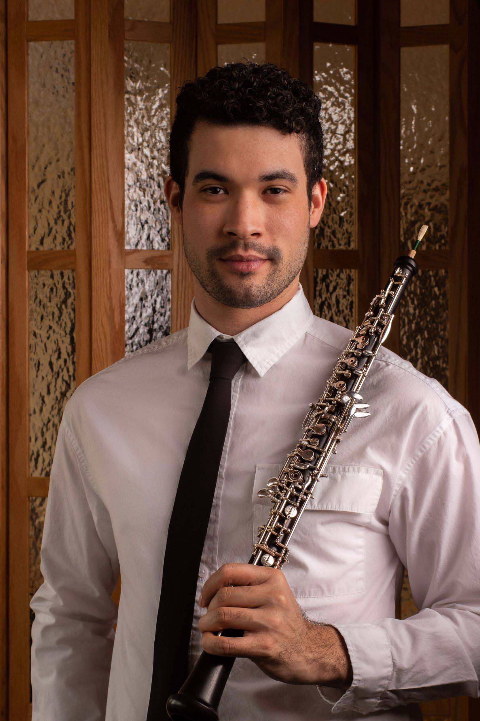 Standing formal studio  portrait of Jeremiah Quarles holding an oboe to his shoulder, wearing a white collared shirt and black tie.