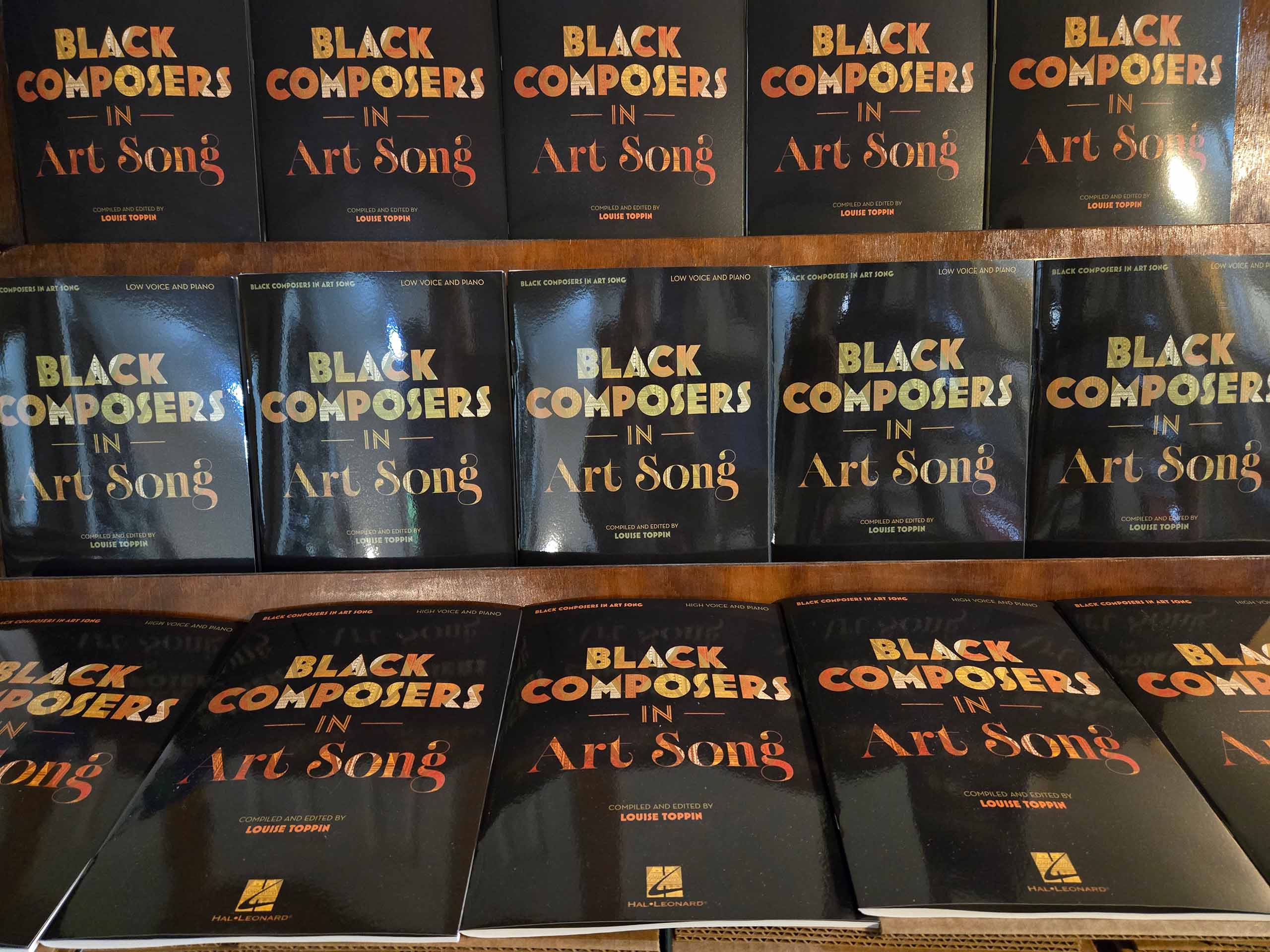 About 15 copies of the publication "Black Composers in Art Song" lay out side by side - with black cover and shiny gold text.