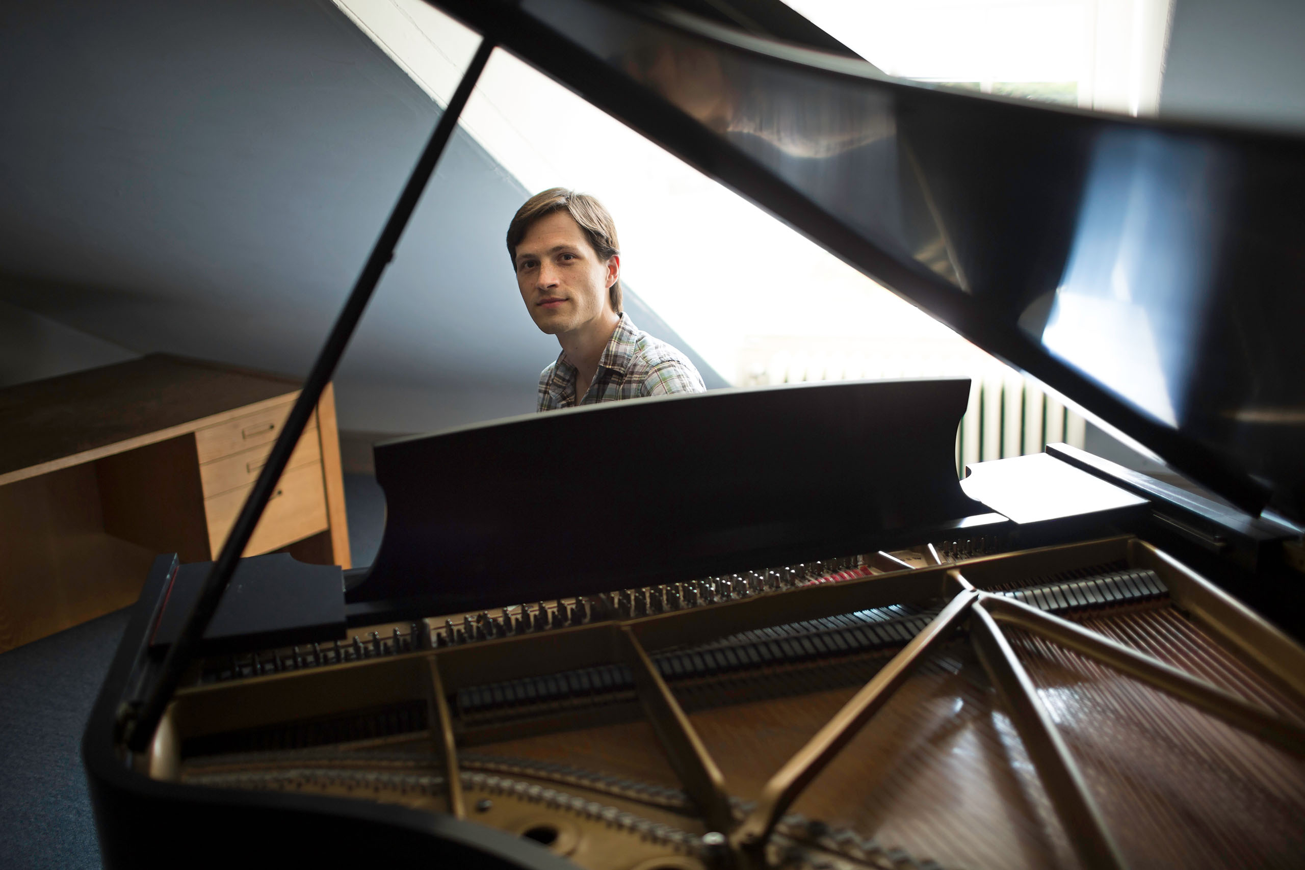 With a piano interior and open lid filling the foreground, Michael Djupstrom looks up from his seat behind the keys for a portrait.