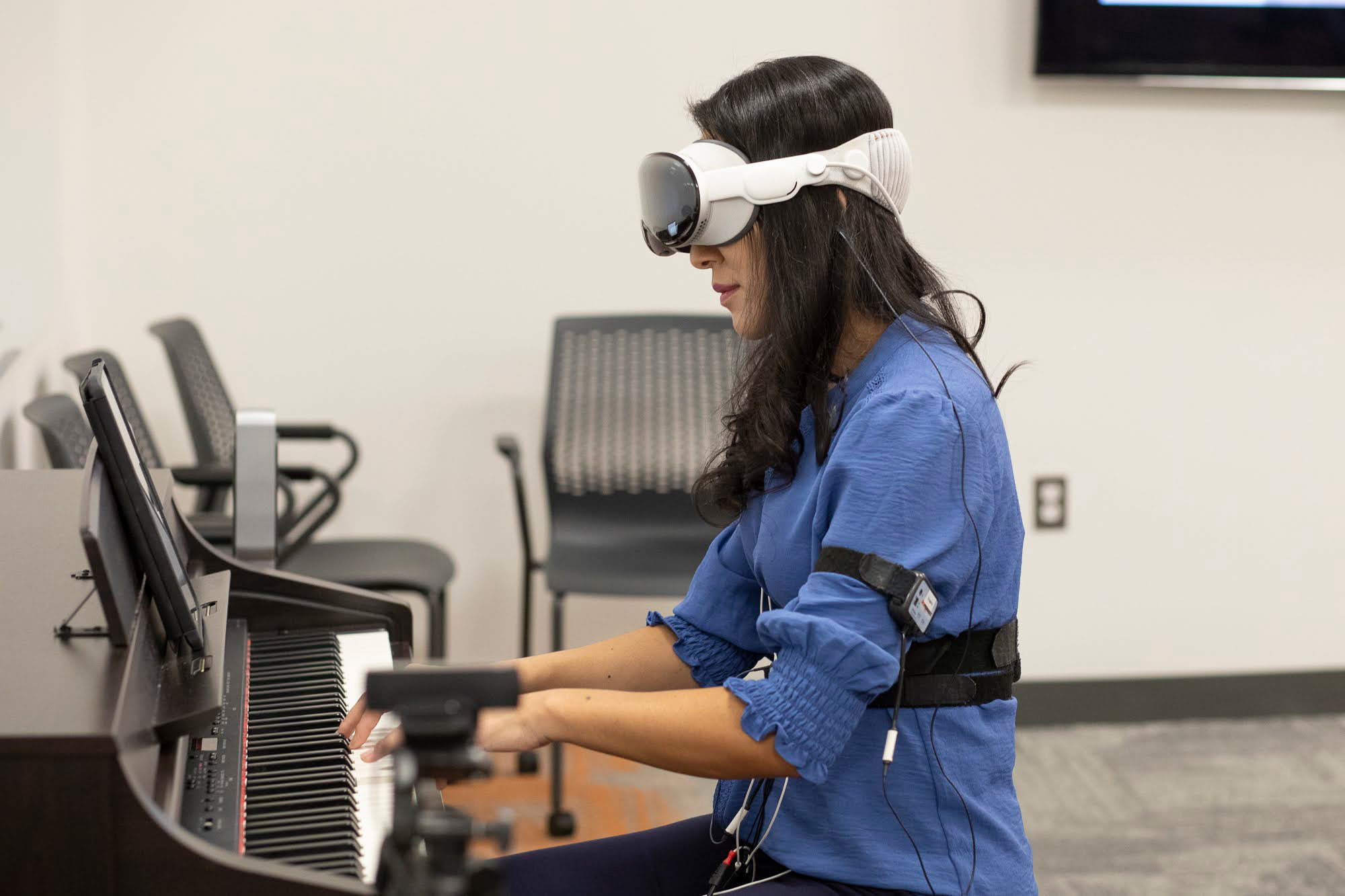 A person plays piano  while wearing an extended reality headset and gear.
