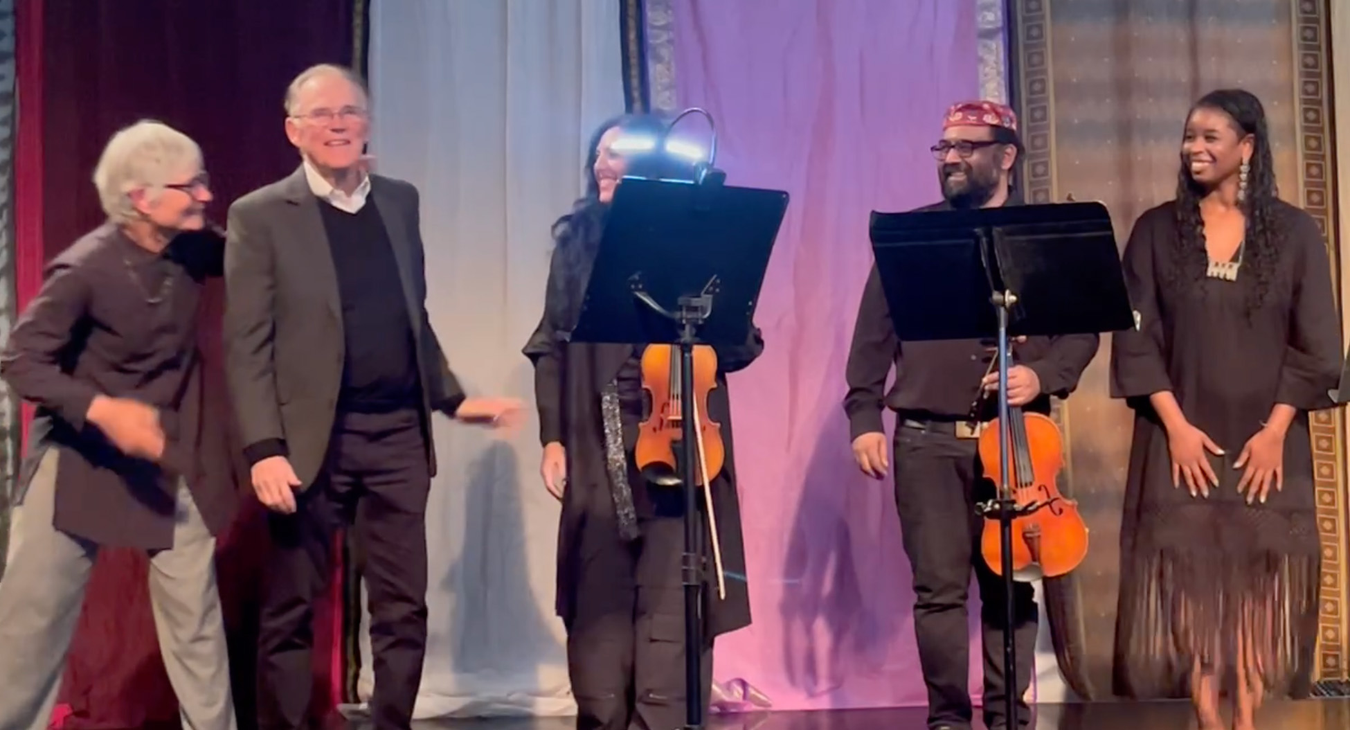 Candid photo of Richard Jennings standing on stage with four other people, all in concert attire. Two music stands are in front of them, and two of the people hold string instruments.