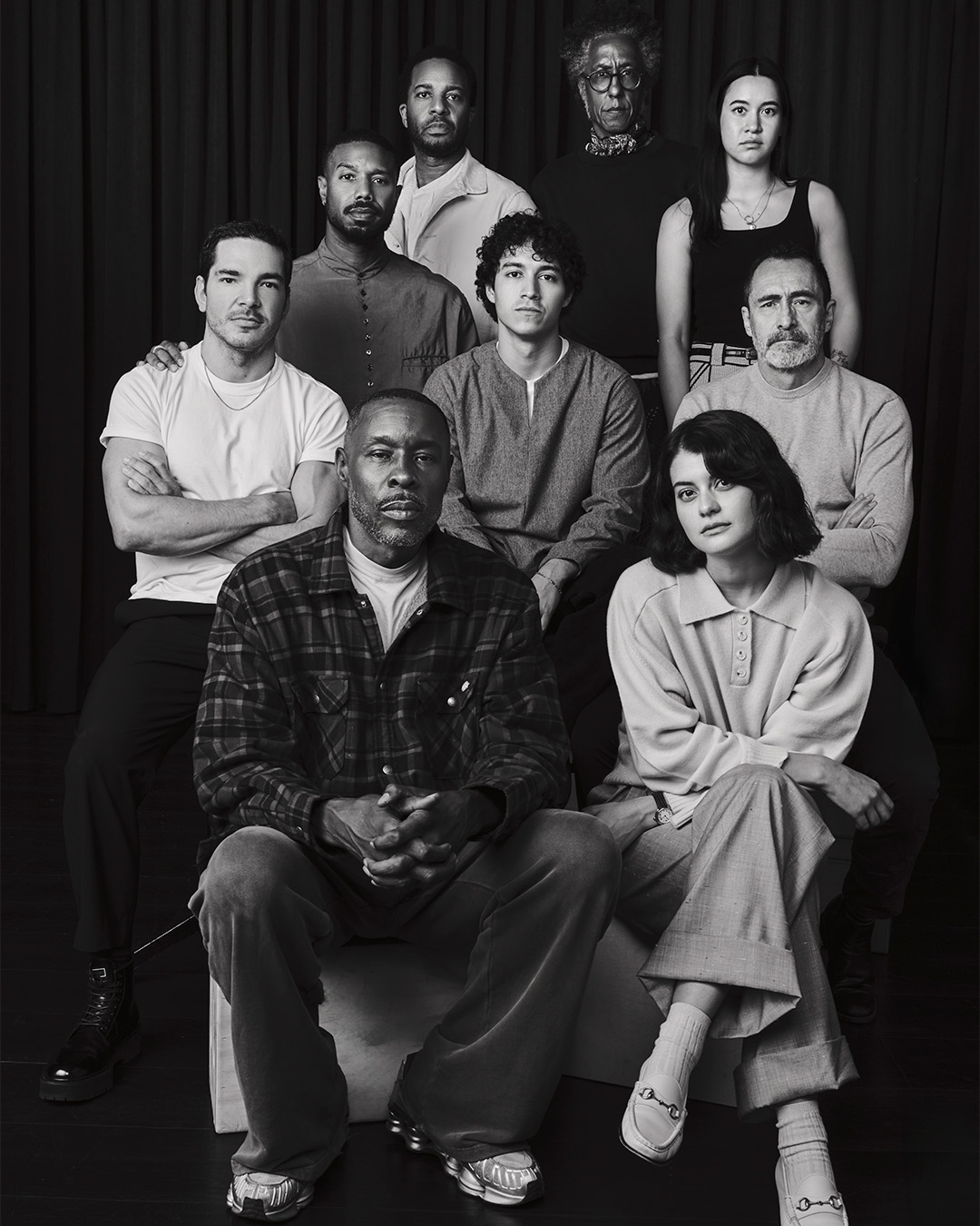 Greyscale portrait of nine people posing together in 4 rows, with serious facial expressions and casual attire.