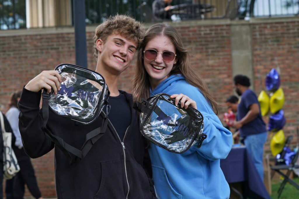 Two students pose smiling and holding up SMTD tote bags at the Welcome Back Carnival.