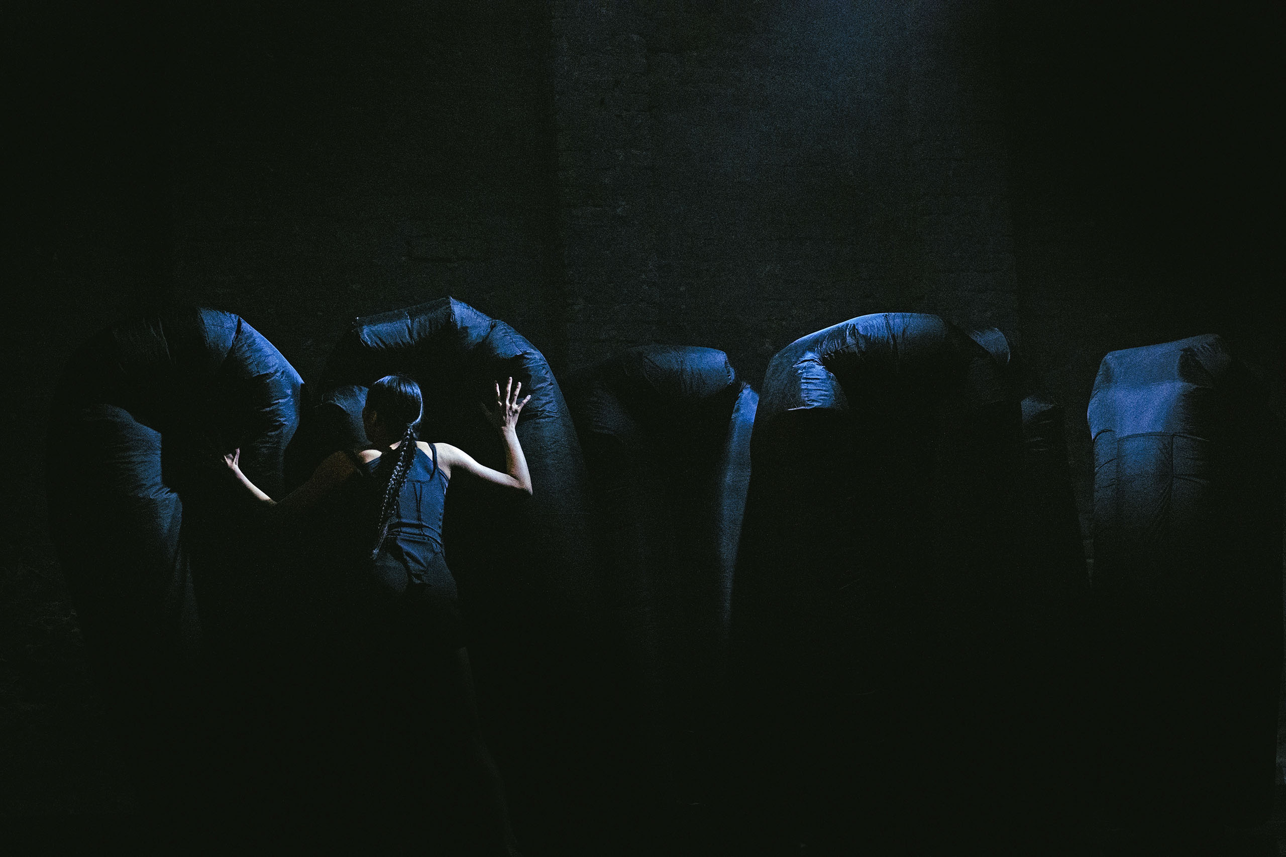 In a dark performance space, a dancer attired in black faces a series of black shapes filled with air.