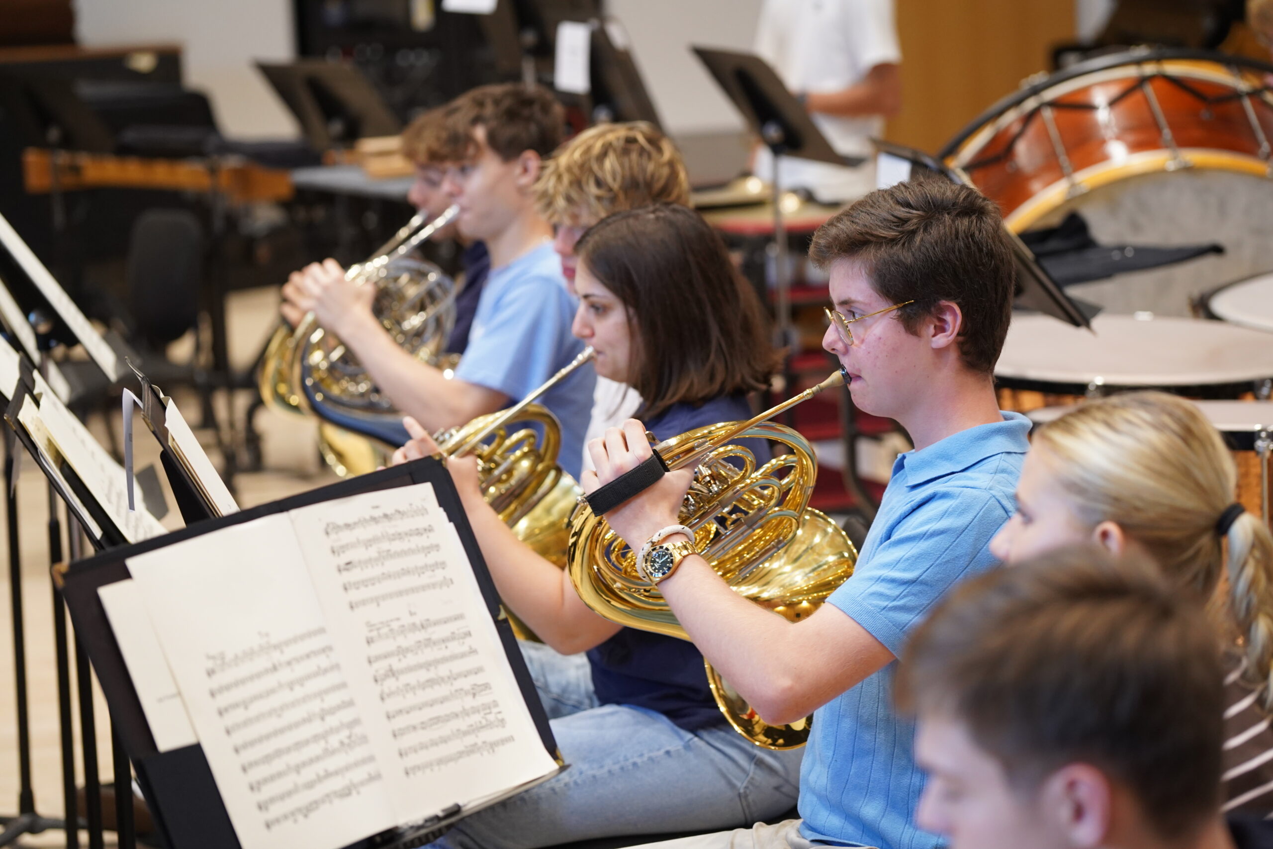 A row of about 4 French horn players seated in a rehearsal.
