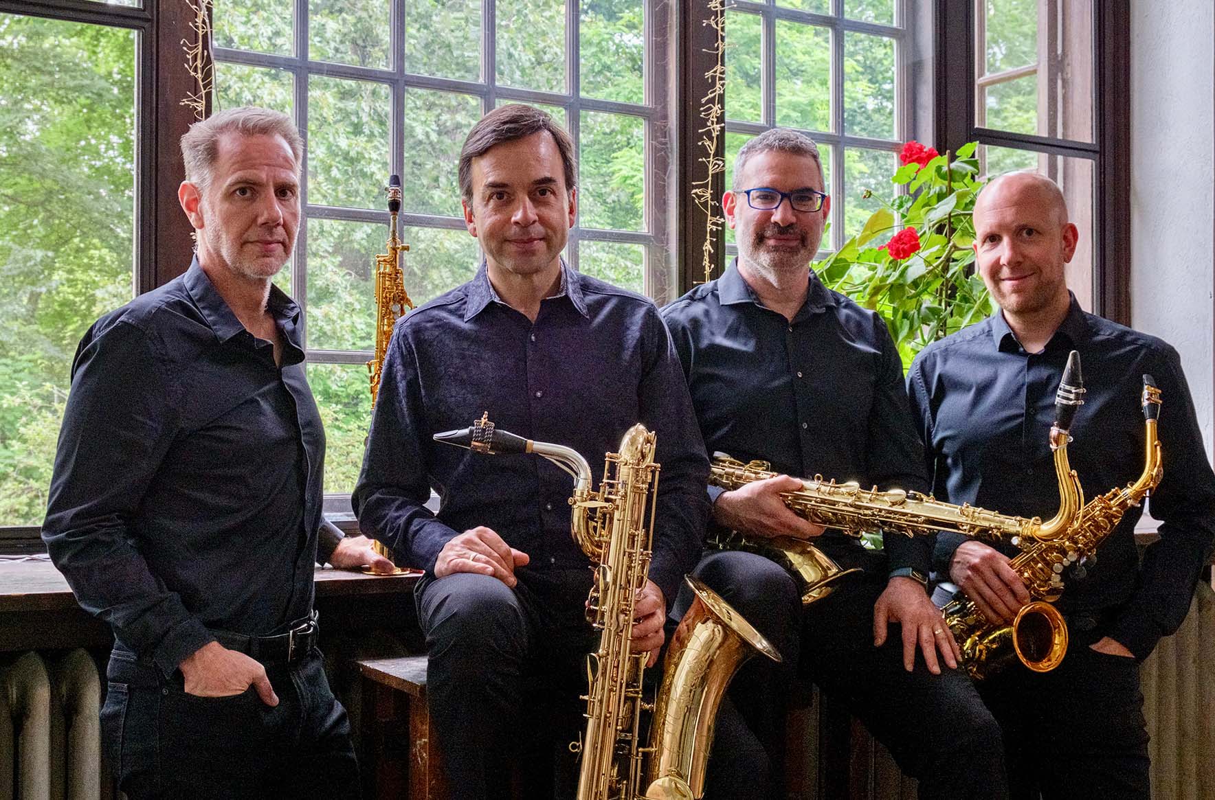 Group portrait of four people, each with a saxophone, and all wearing black.